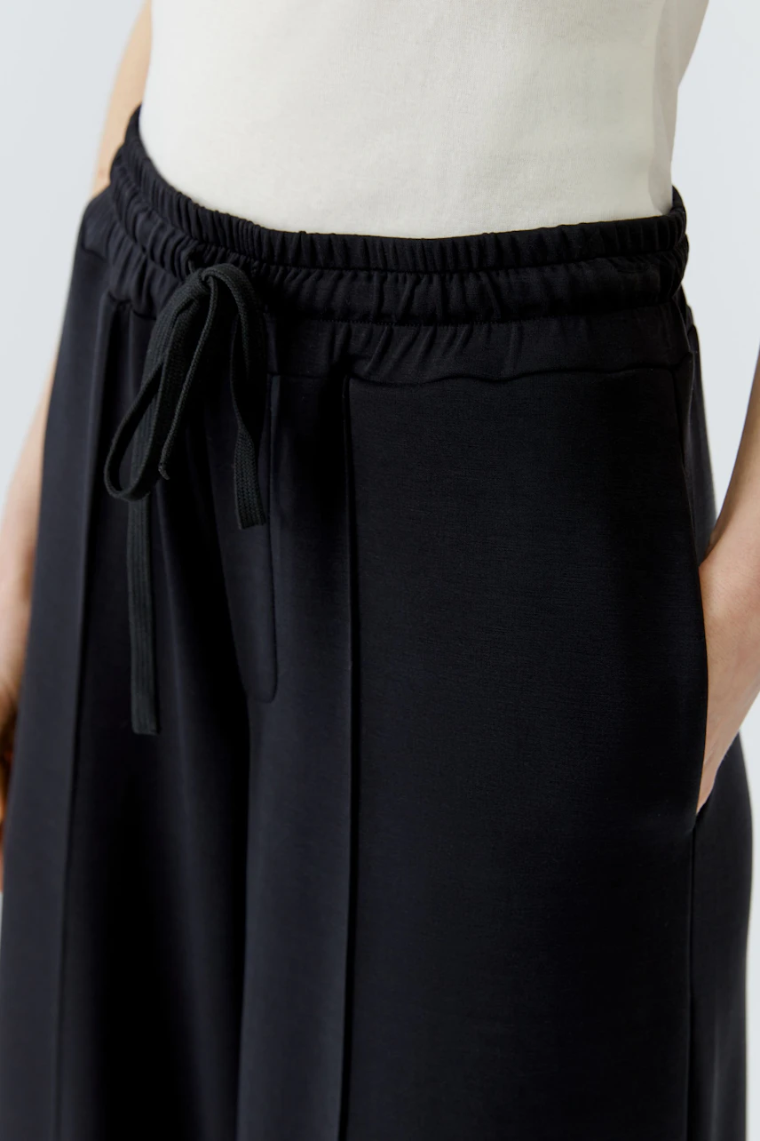Schwarze Marlenehose mit elastischem Bund und Kordelzug, getragen von einer Frau in weißem Oberteil.