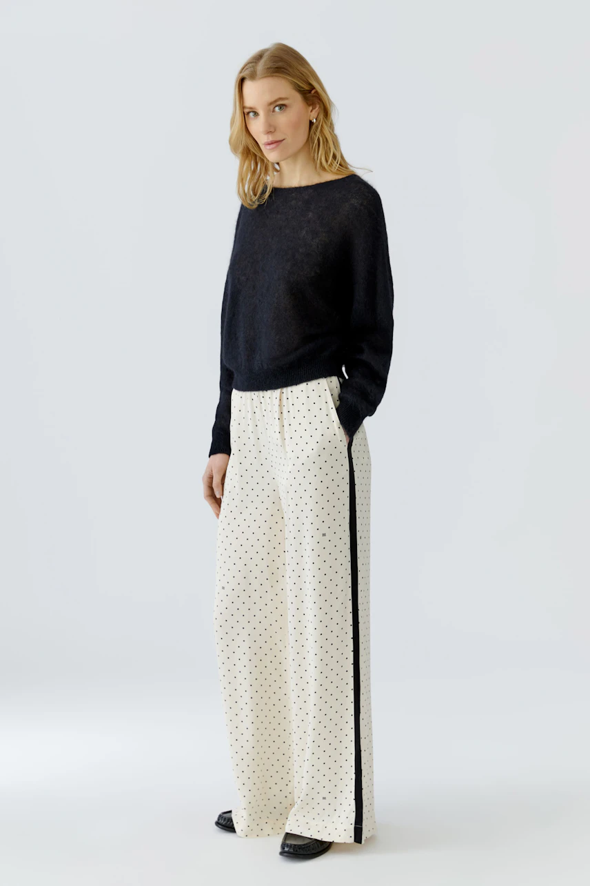 Damen-Hose: Frau in weißer Hose mit schwarzen Punkten und schwarzem Pullover, lässig und modern.