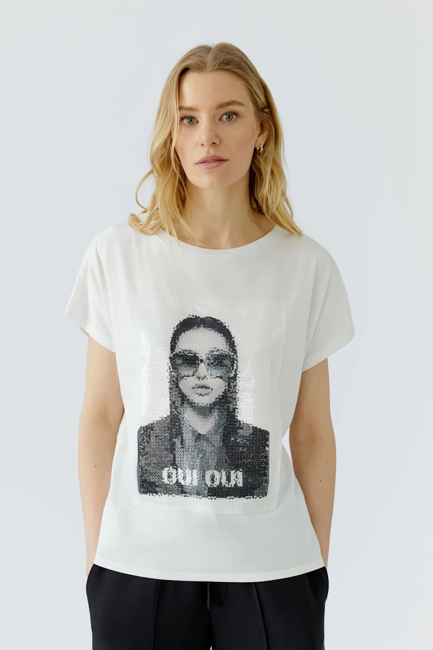 Casual women's T-shirt: Woman in white T-shirt with graphic print, relaxed fit, and black pants.