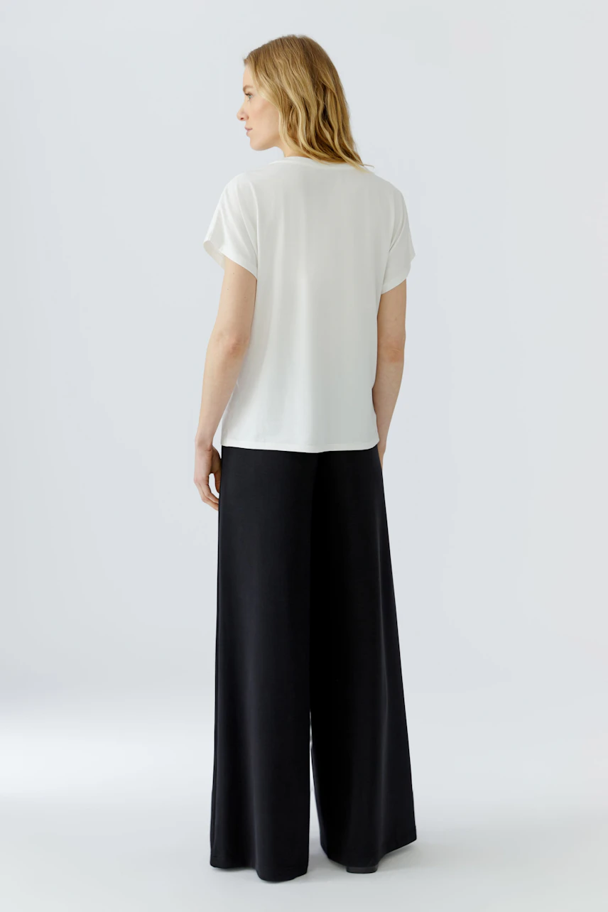 Casual women's T-shirt: Woman in a white T-shirt and black wide-leg pants, viewed from the back.