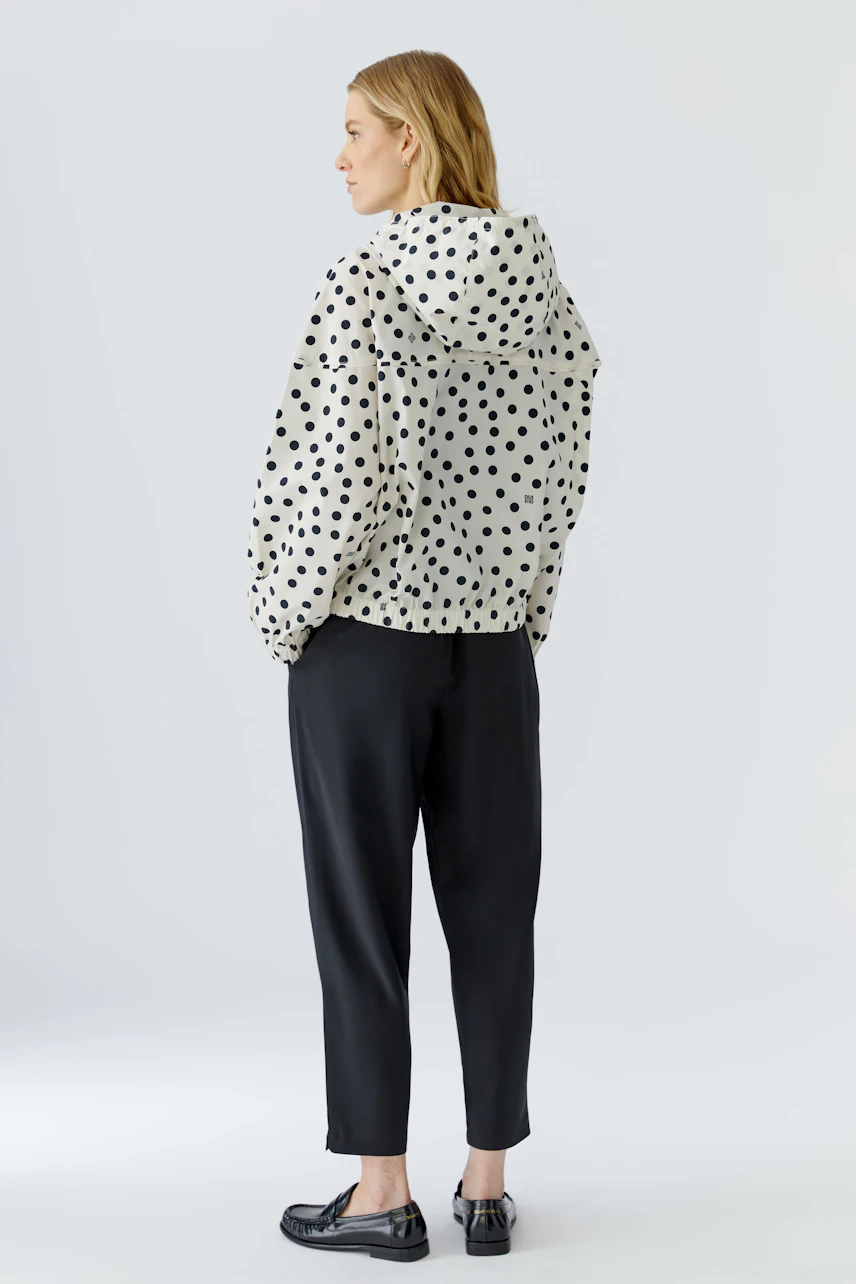 Damen-Blouson: Frau im gepunkteten Blouson, schwarze Hose, seitlicher Blick, lässiger Stil.