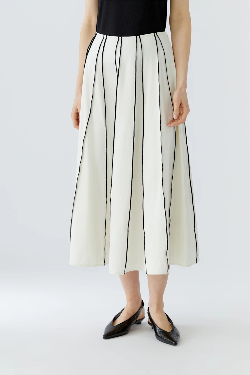 A-line skirt: Woman in a black top and white skirt with vertical stripes, wearing black shoes.