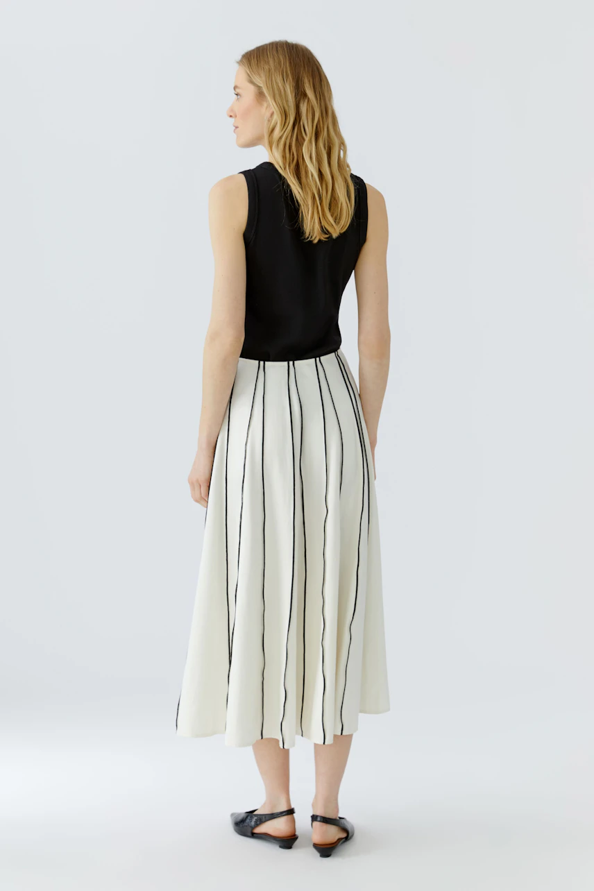 A-line skirt: Woman in a black top and white A-line skirt with vertical stripes, standing confidently.