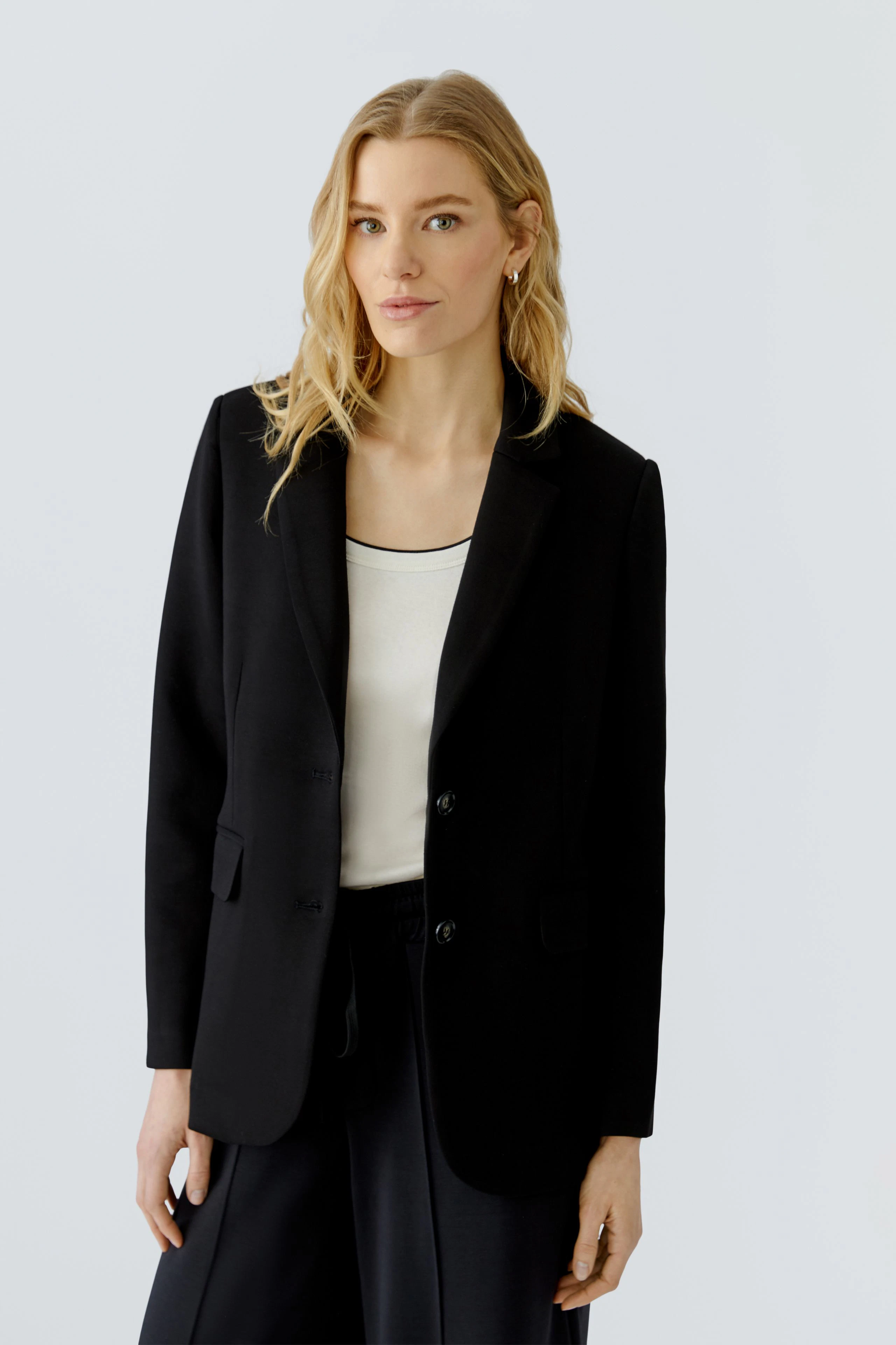 Schwarzer Damen-Blazer: Frau im klassischen Blazer mit weißem Top und dunkler Hose, schlicht und zeitlos.
