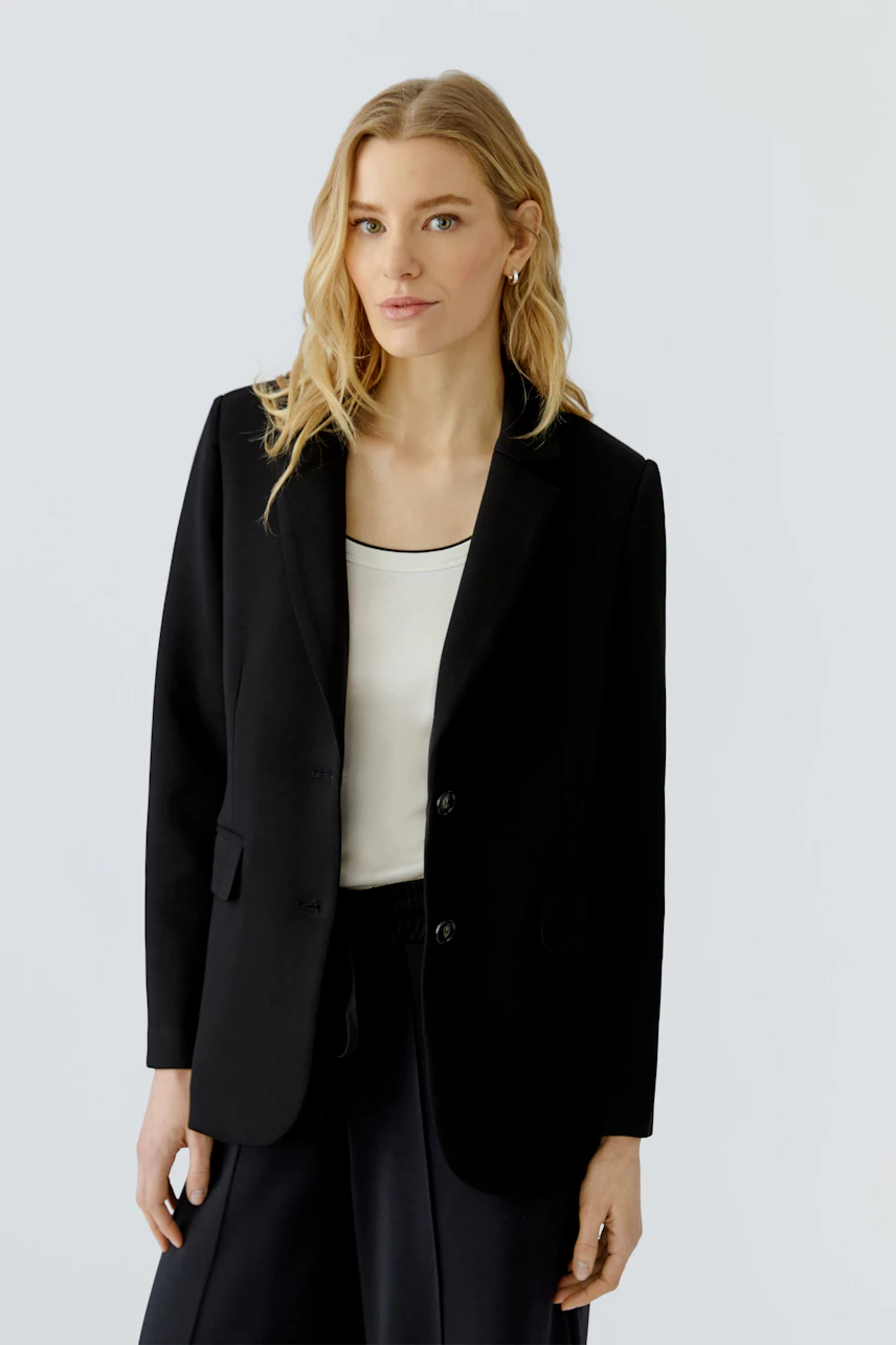 Schwarzer Damen-Blazer: Frau im klassischen Blazer mit weißem Top und dunkler Hose, schlicht und zeitlos.