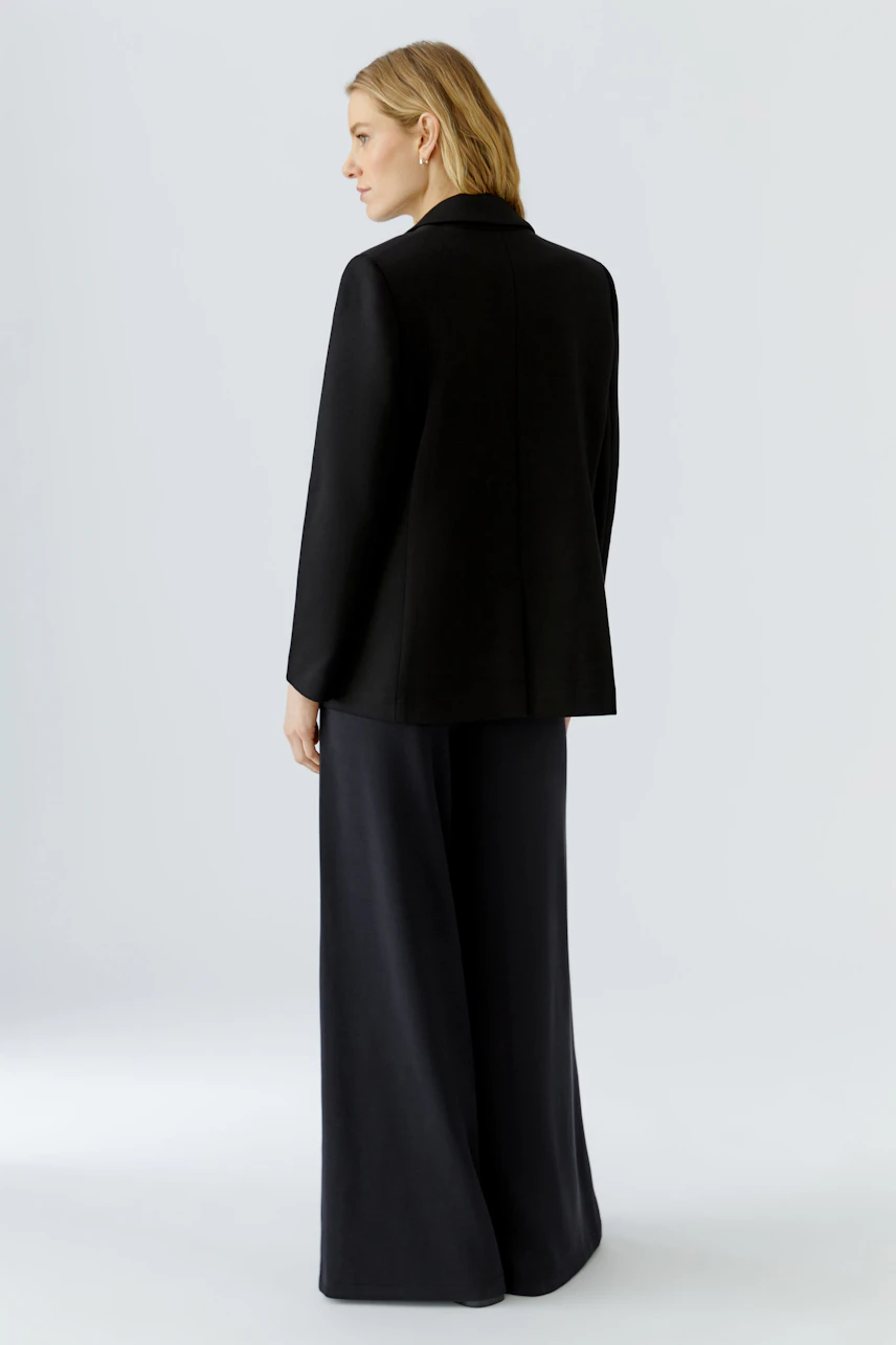 Schwarzer Damen-Blazer: Frau im lässigen Blazer und weiter Hose, von hinten gesehen.