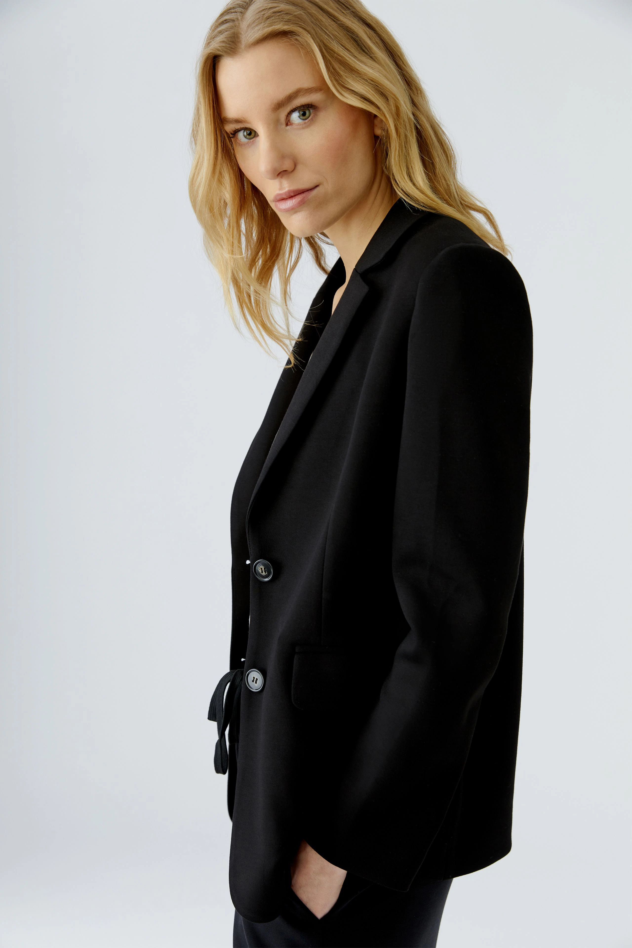 Schwarzer Damen-Blazer: Frau im klassischen Blazer mit zwei Knöpfen, seitlich stehend, schaut direkt.