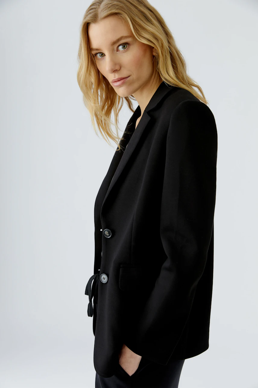Schwarzer Damen-Blazer: Frau im klassischen Blazer mit zwei Knöpfen, seitlich stehend, schaut direkt.