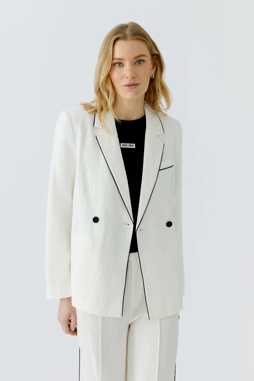 Weißer Damen-Blazer: Frau im weißen Blazer mit schwarzen Details und passender Hose, lässig und modern.
