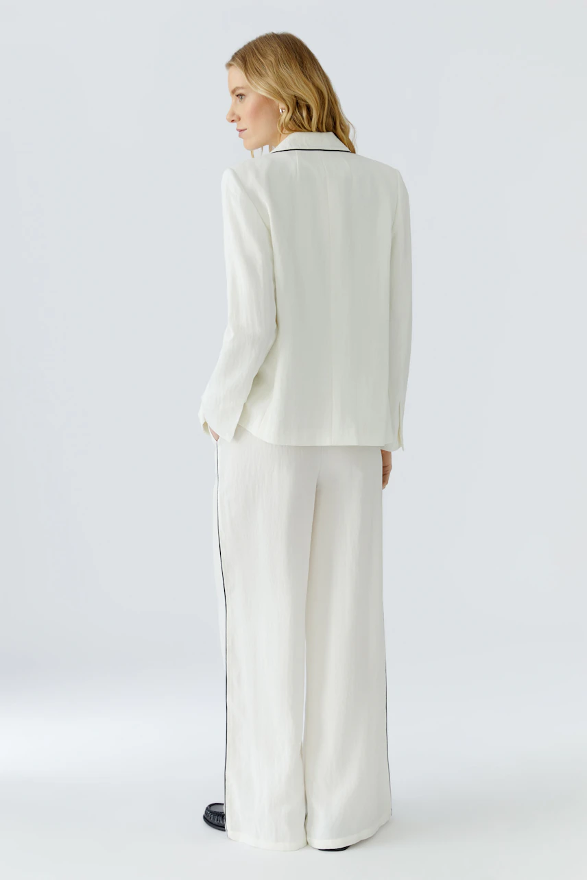 Weißer Damen-Blazer: Frau im weißen Blazer mit passender Hose, seitlich stehend, schlicht und modern.