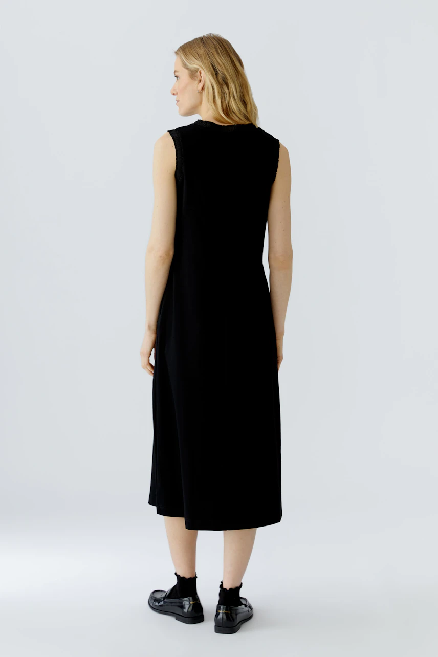 Casual midi dress: Woman in sleeveless black dress, standing with relaxed posture, wearing black sneakers.