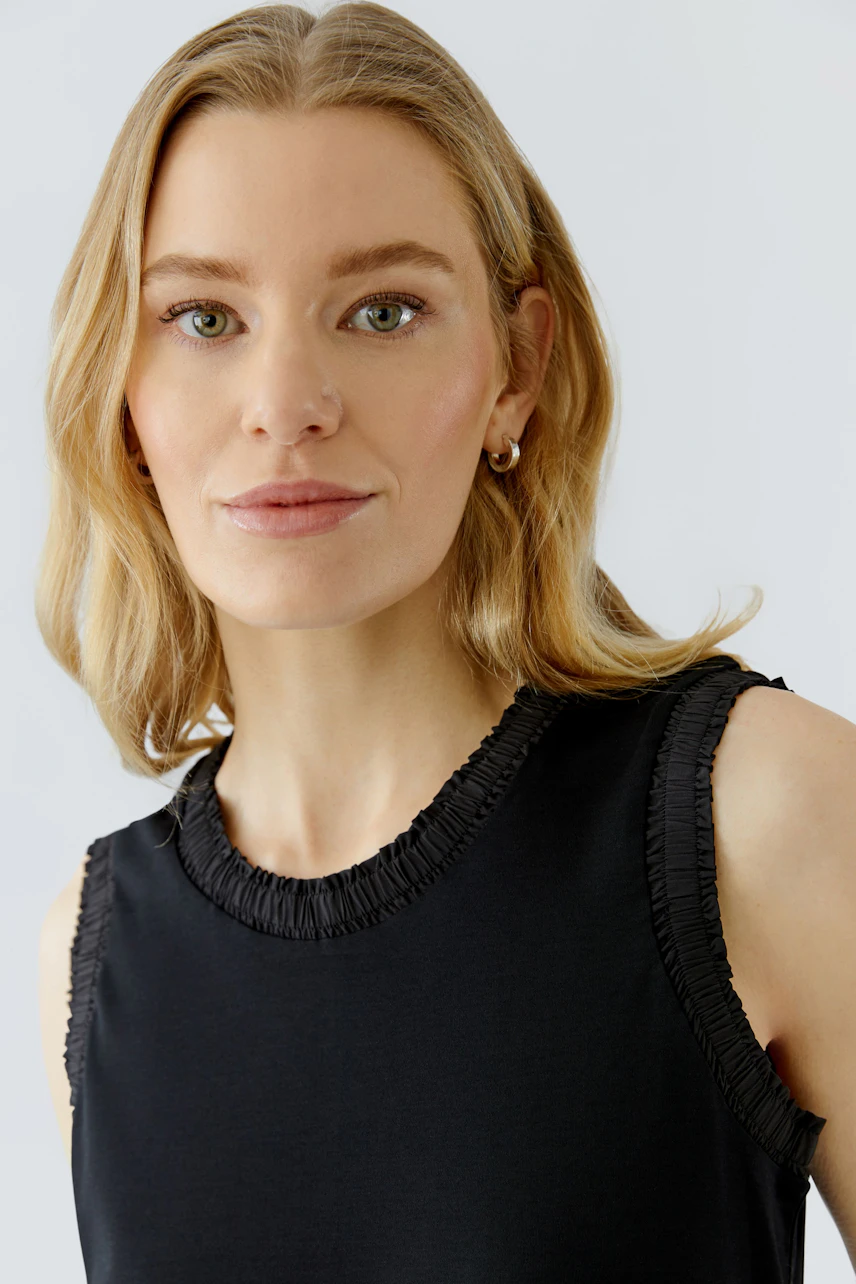 Woman in a sleeveless black midi dress with ruffled edges, looking confidently at the camera.