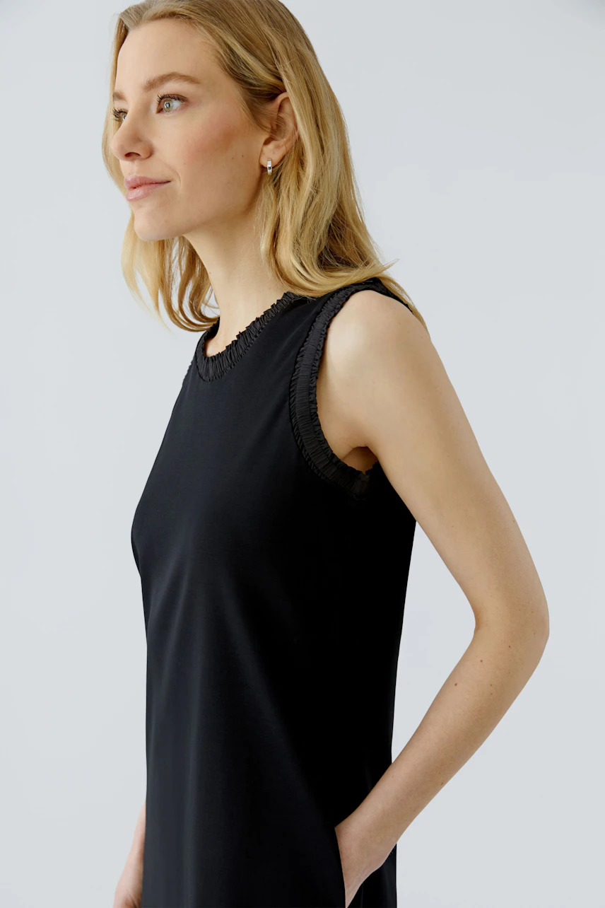 Casual midi dress: Woman in sleeveless black dress with subtle details, looking confidently to the side.
