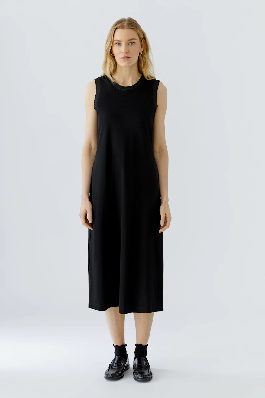 Casual black midi dress: Woman in sleeveless black dress with relaxed fit and simple design.
