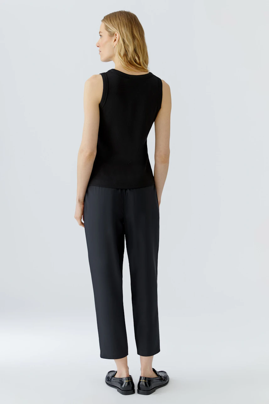 Black tank top: Woman in a sleeveless black top and dark pants, viewed from the back.