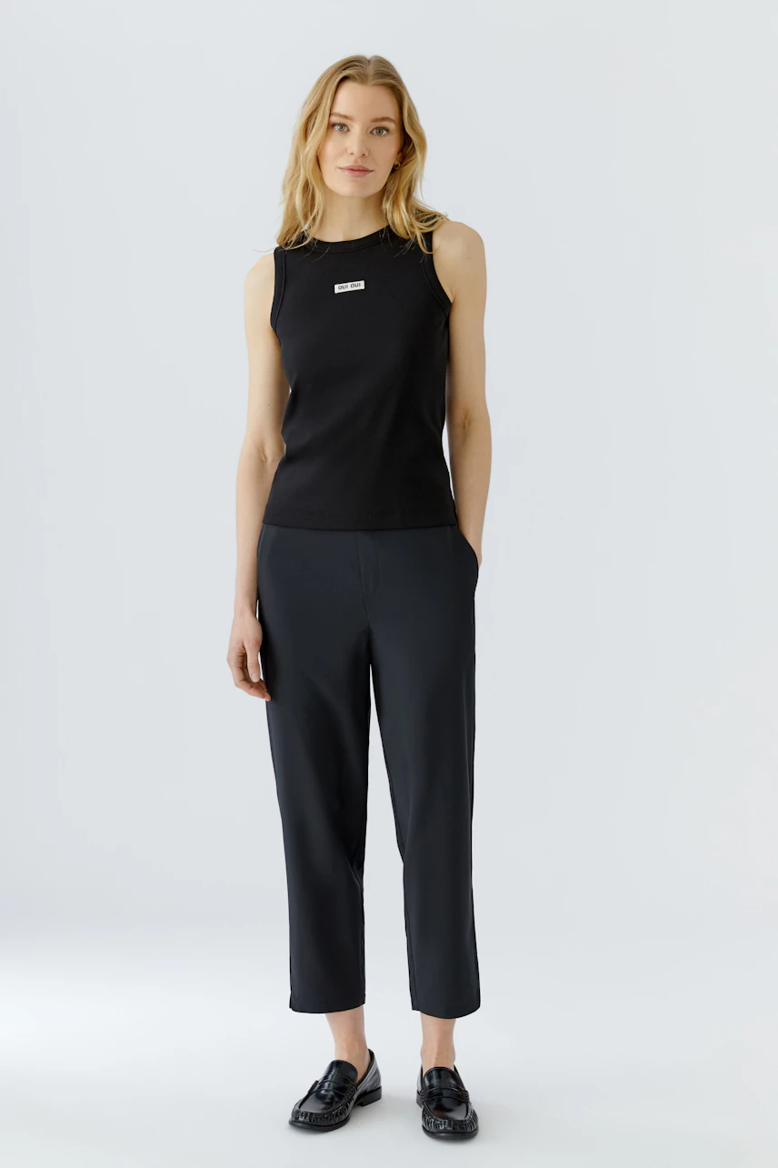 Casual tank top: Woman in a black tank top and dark pants, standing confidently.