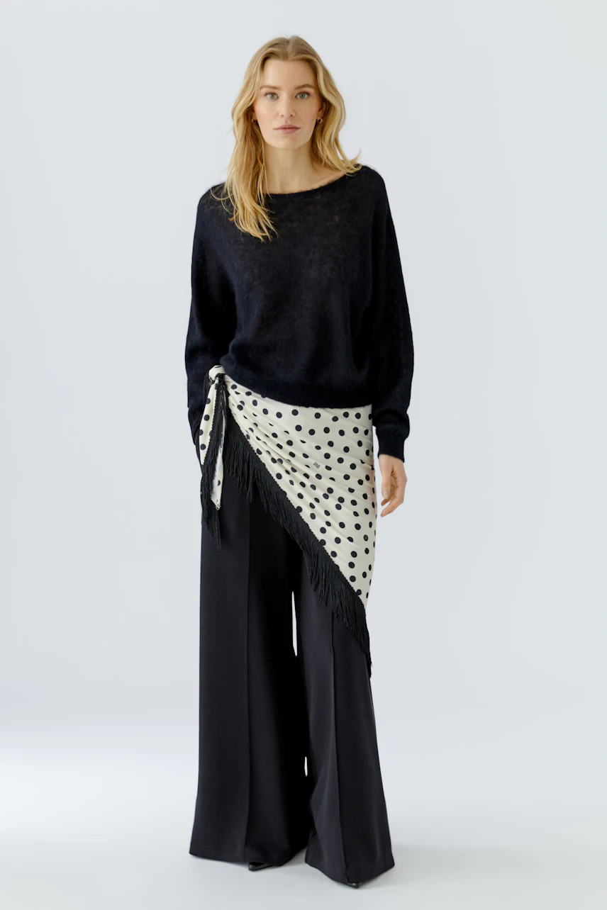 Woman in black pullover with polka dot scarf tied at waist, paired with wide-leg pants.