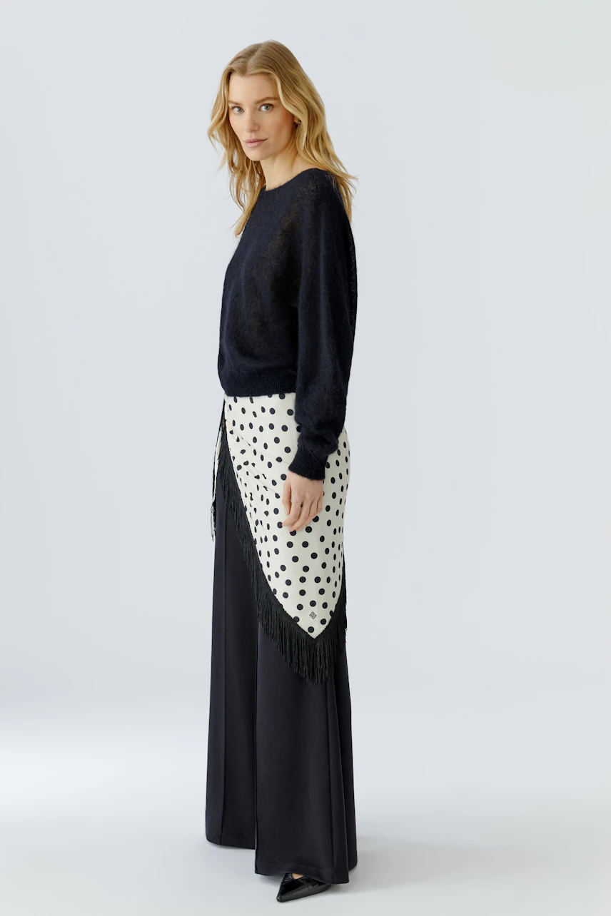 Woman in black pullover with polka dot scarf, wearing wide-leg pants, looking confidently.