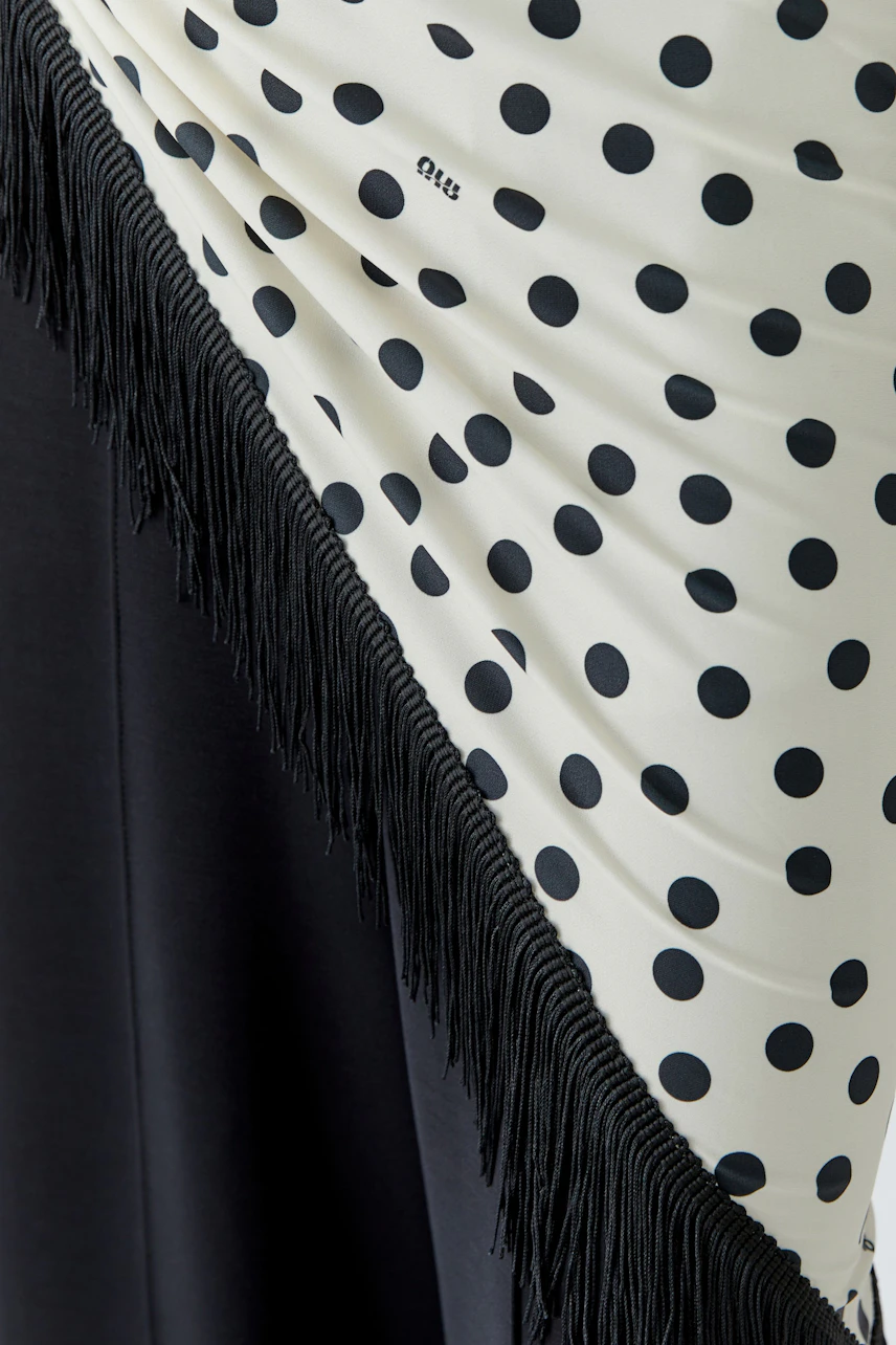 Polka dot scarf with black fringe detail, draped over a dark fabric. No model visible.
