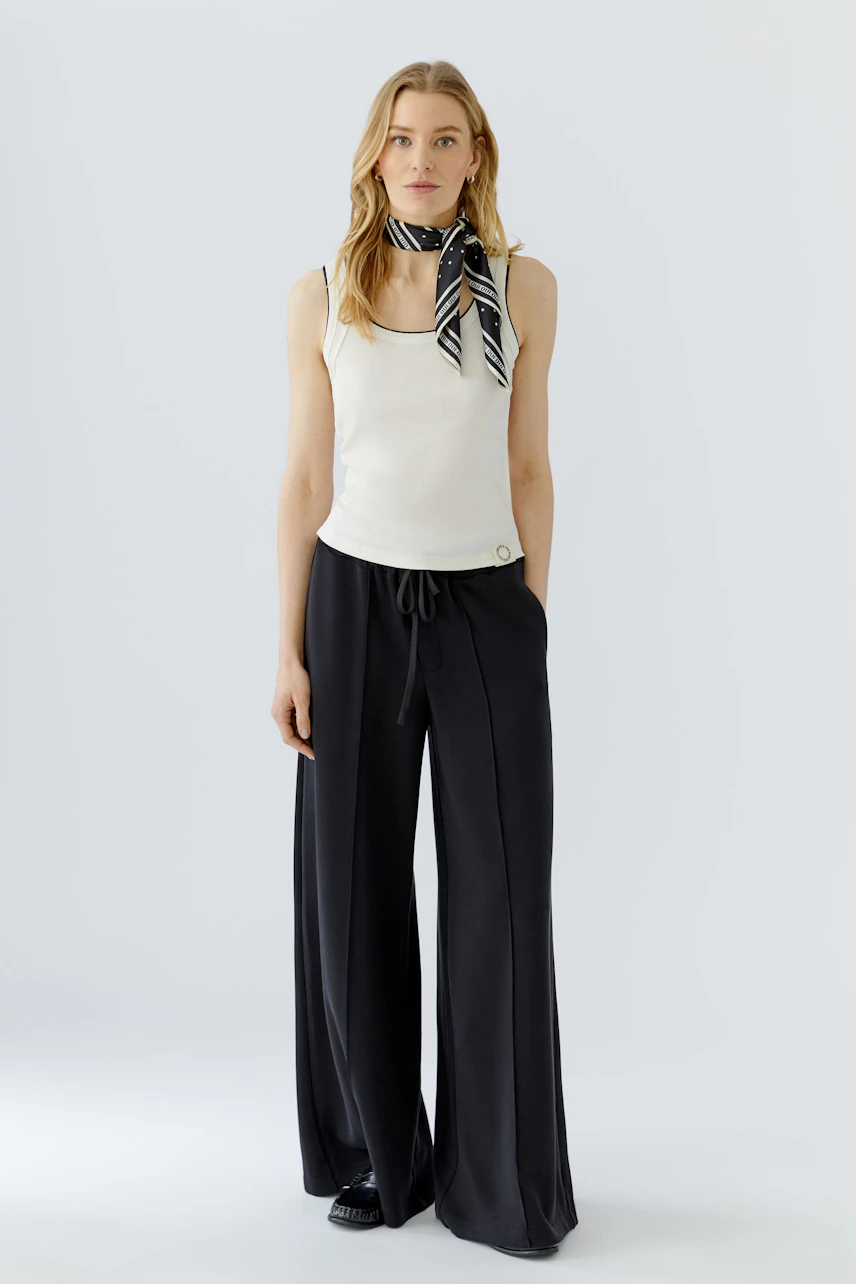 Casual scarf: Woman in a white tank top with a black and white striped scarf, paired with wide-leg pants.