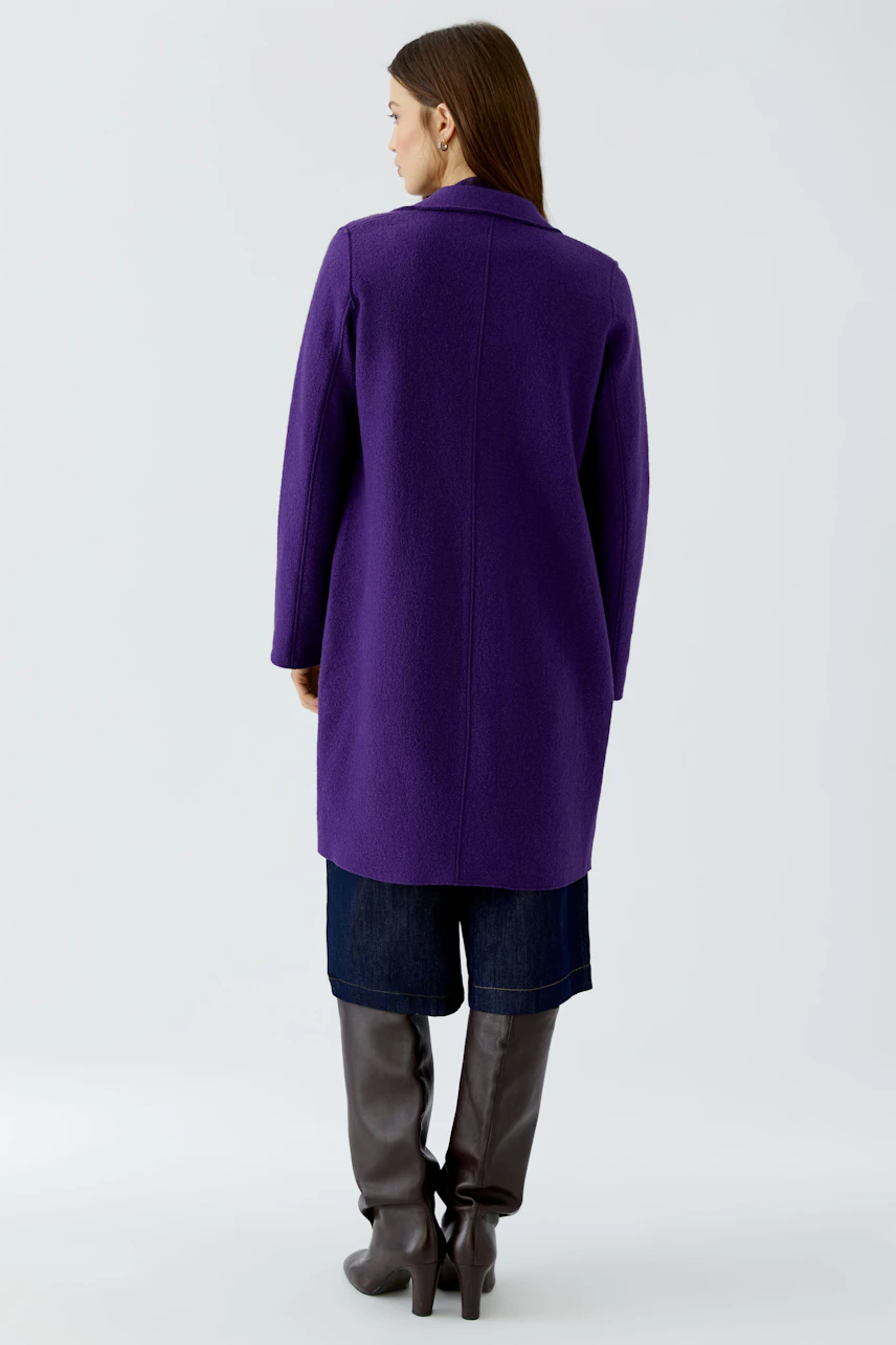 Woman in a purple wool coat, back view, paired with dark jeans and tall boots.