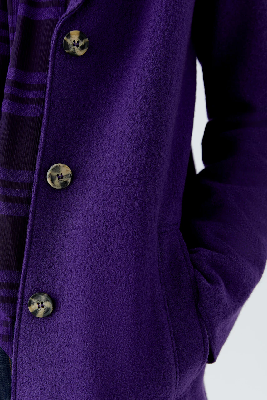 Purple wool coat: Close-up of a woman's hand in pocket, showcasing textured fabric and large buttons.