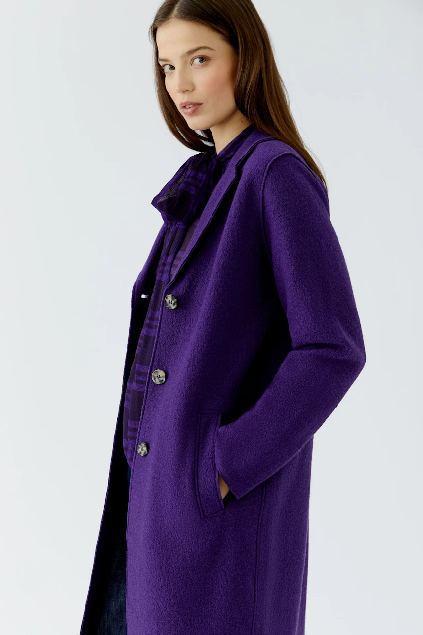 Woman in a purple wool coat, standing confidently with hands in pockets, wearing a matching shirt.