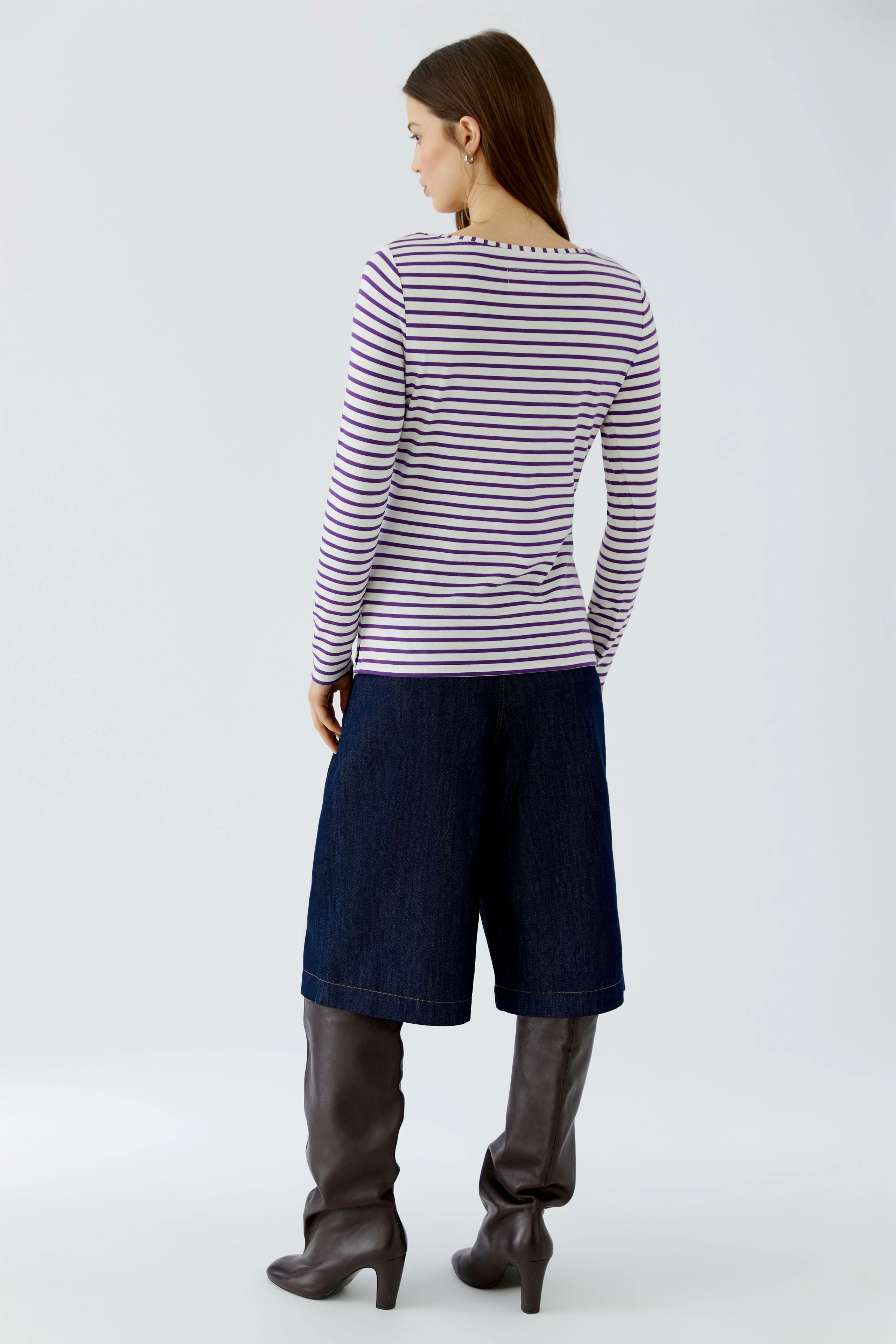 Striped long-sleeve shirt: Woman in casual striped shirt, denim culottes, and knee-high boots, facing away.