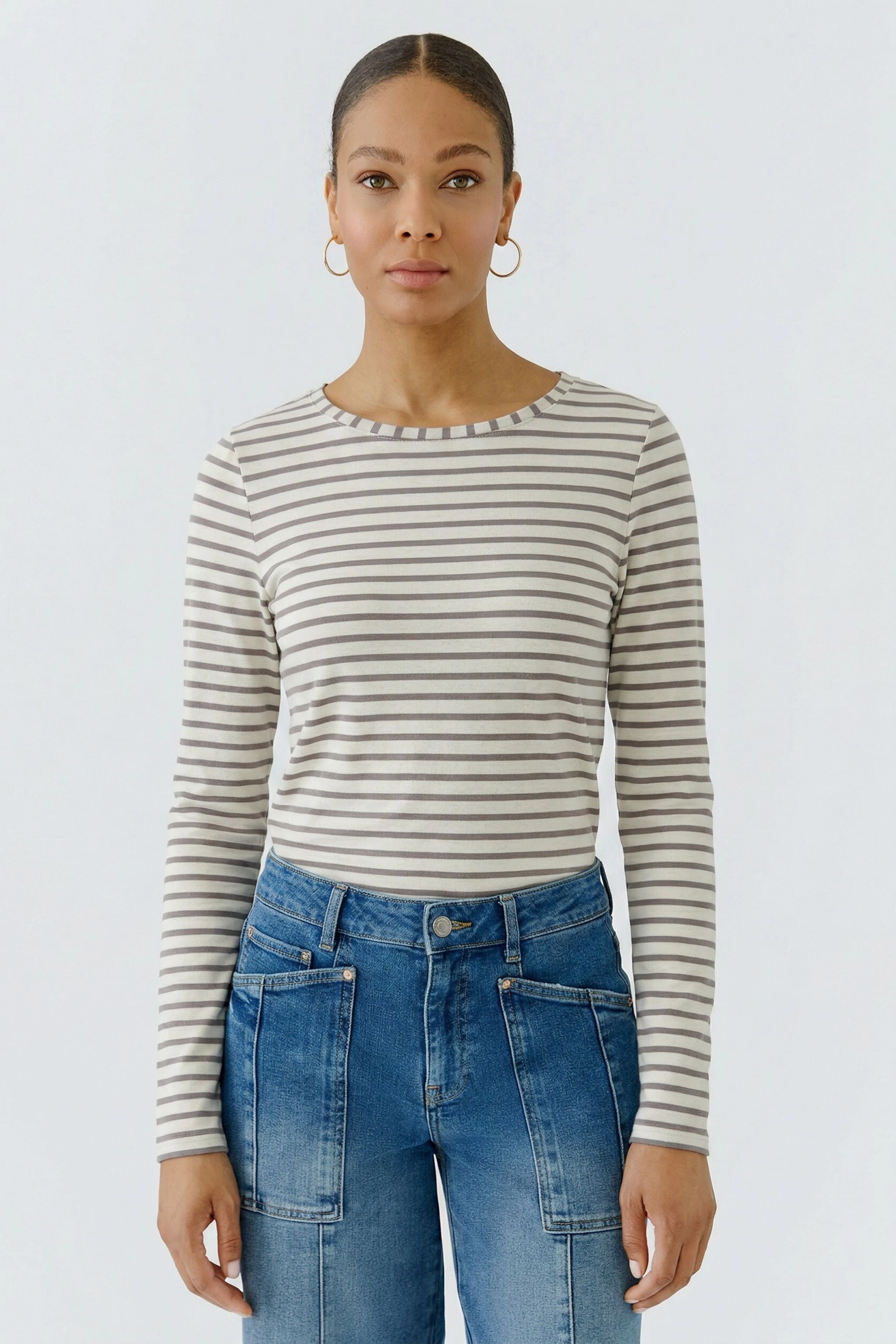 Striped long-sleeve shirt: Woman in casual striped shirt and denim jeans, looking confidently ahead.