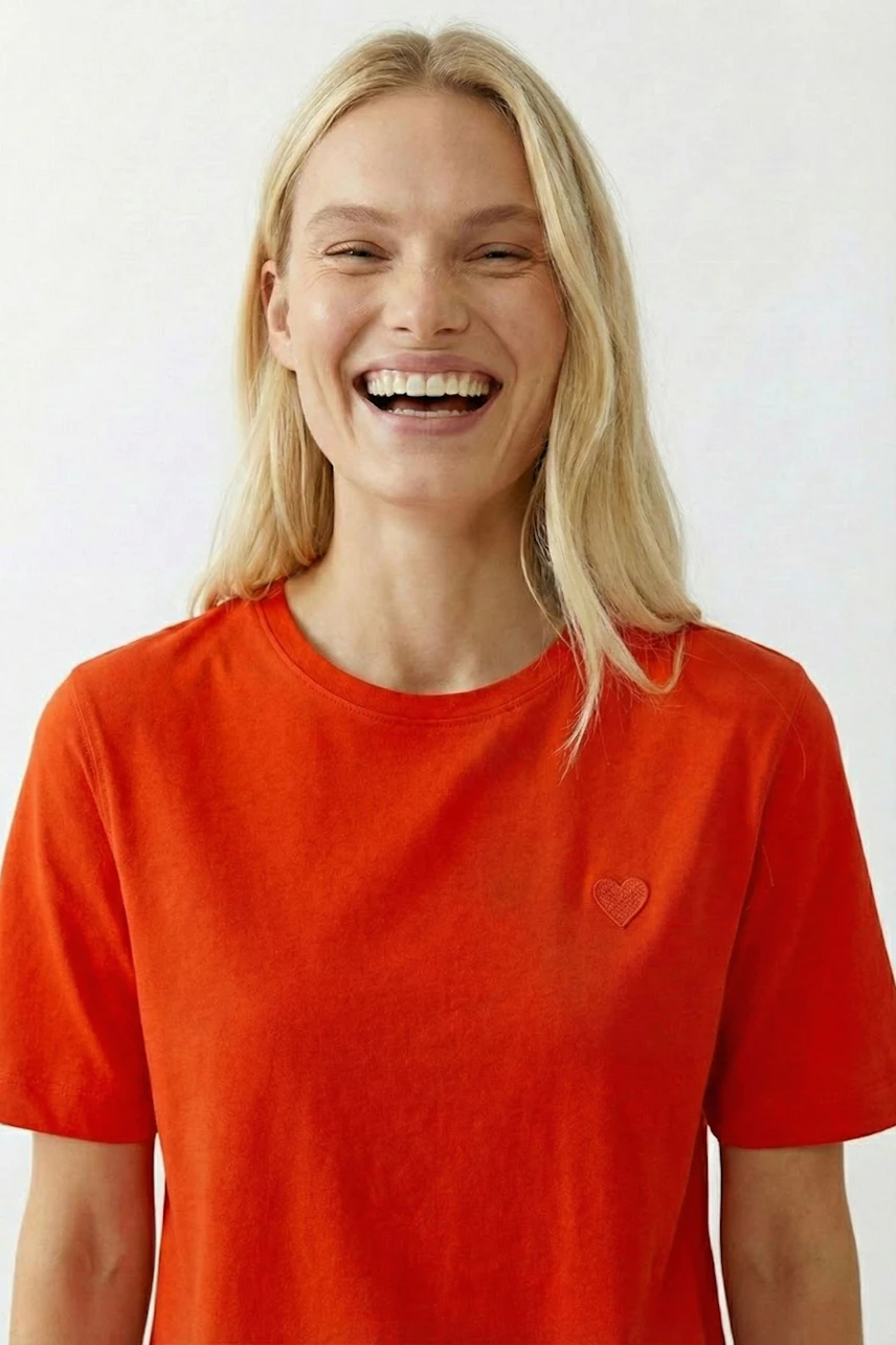 Casual women's T-shirt: Smiling woman in a bright orange tee with a heart detail.