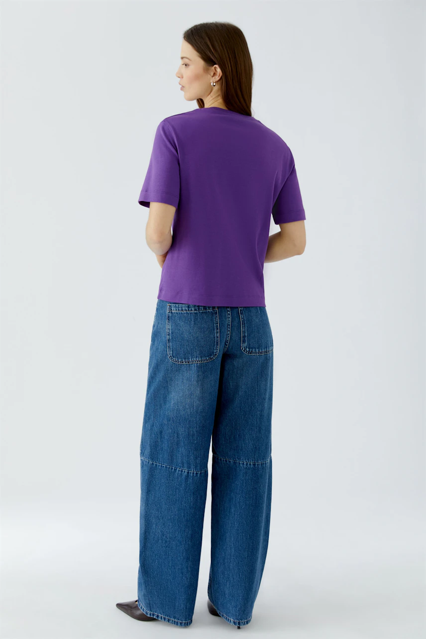 Lässiges Damen-T-Shirt: Frau im lila T-Shirt und blauer Jeans, von hinten gesehen.
