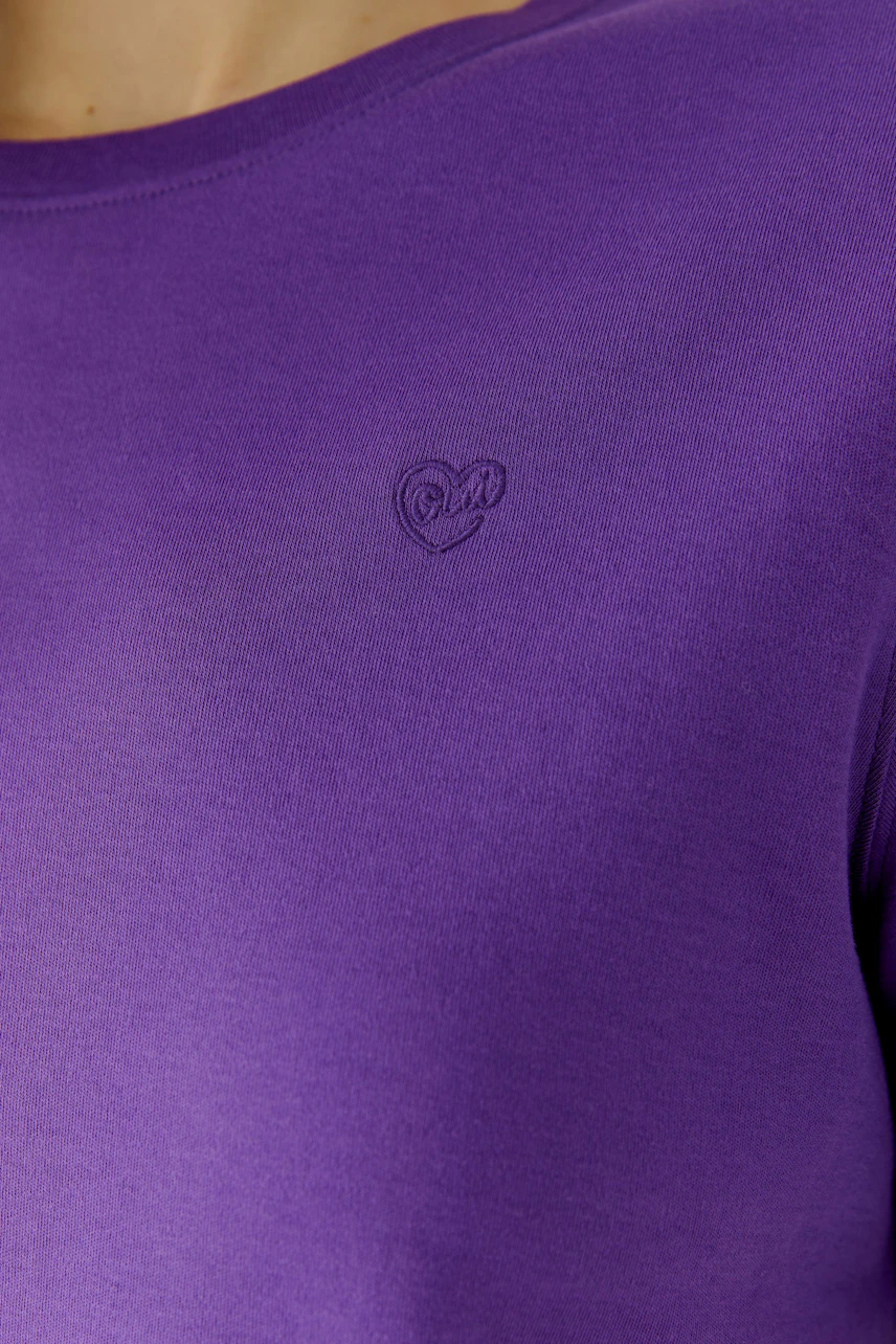 Lila T-Shirt: Frau trägt schlichtes lila T-Shirt mit kleinem Logo auf der Brust.