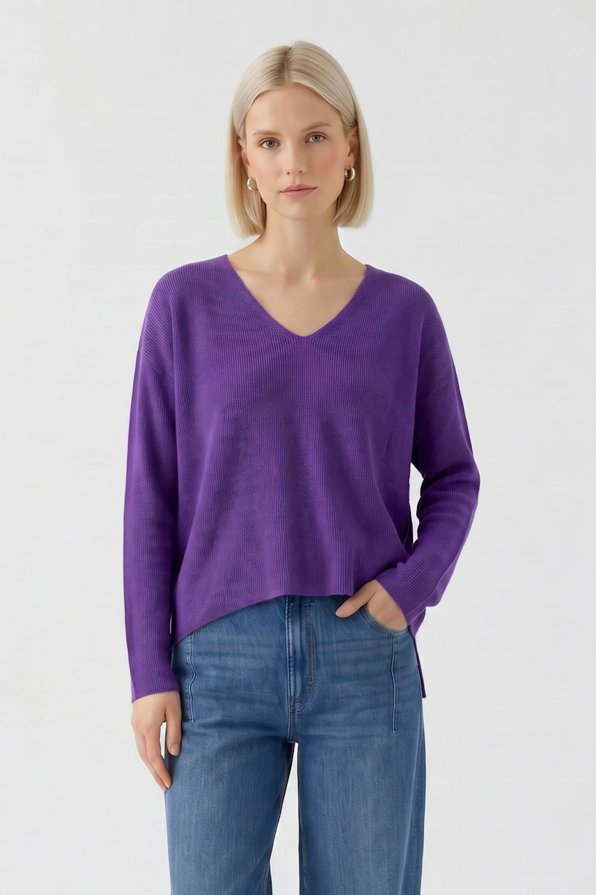 Casual women's pullover: Woman in a purple V-neck pullover and blue jeans, standing confidently.
