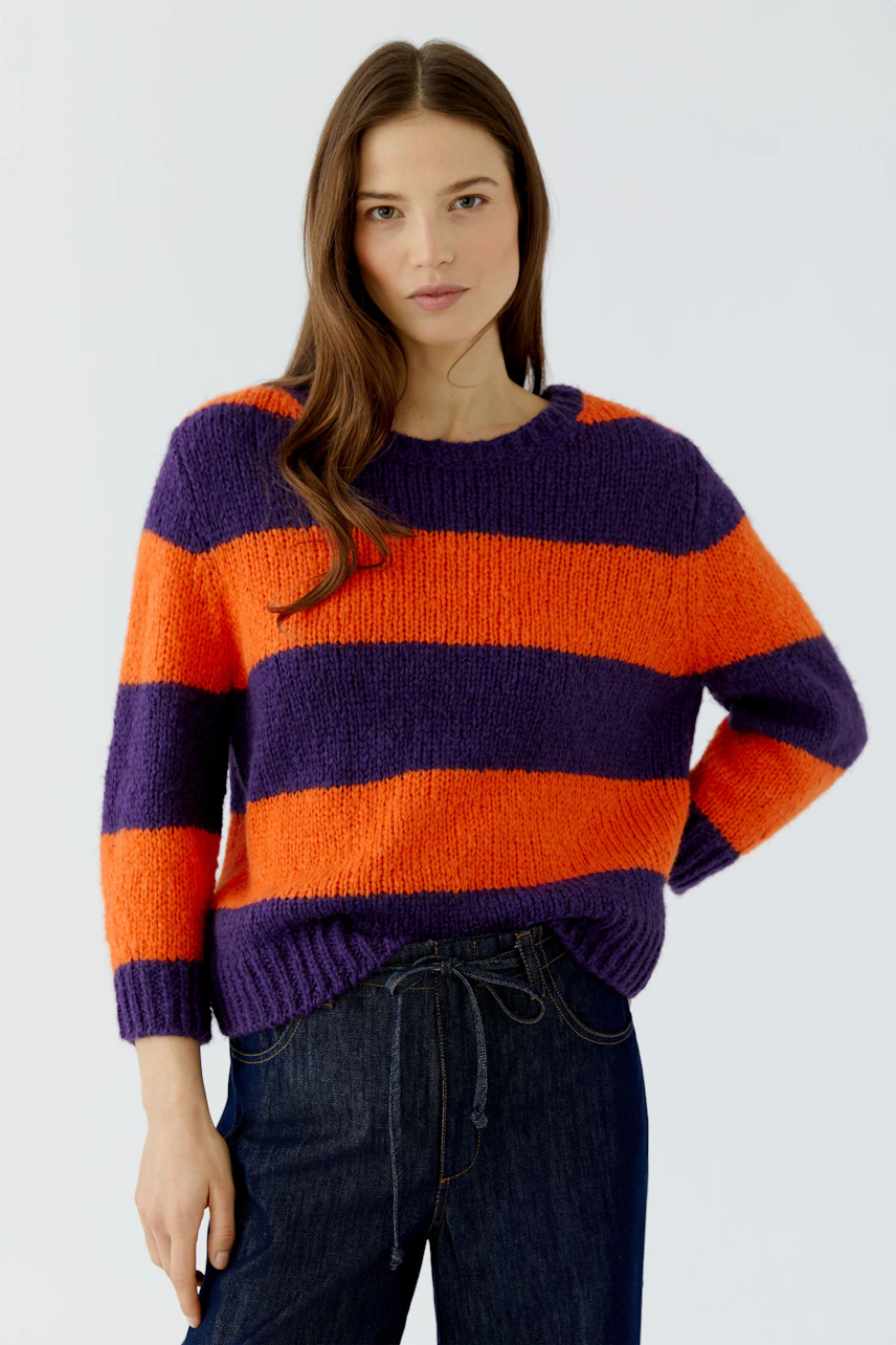 Casual women's pullover: Woman in vibrant orange and purple striped pullover with relaxed fit.