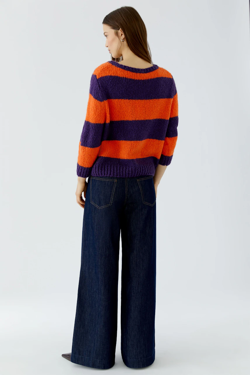 Casual women's pullover: Woman in orange and purple striped pullover with wide-leg jeans, looking relaxed.