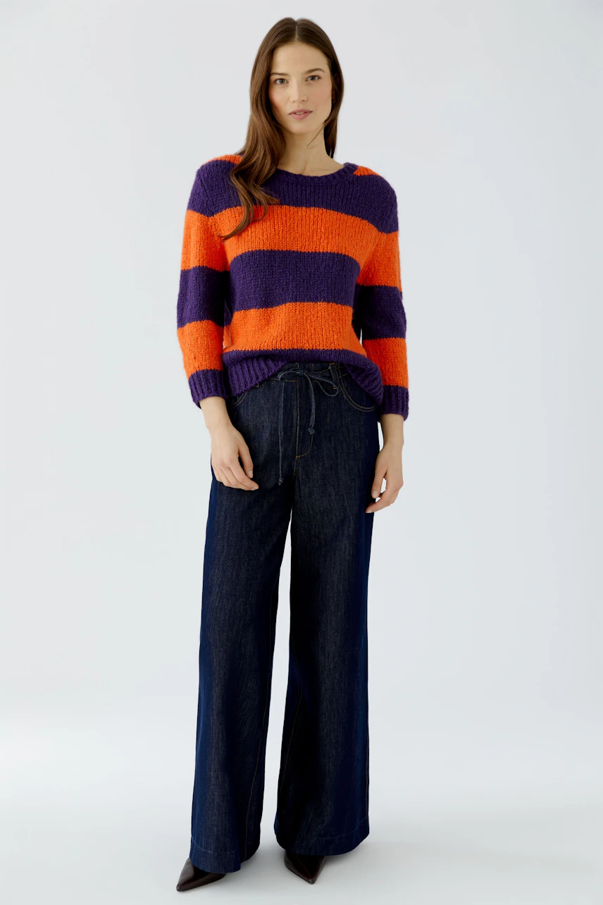Casual women's pullover: Woman in vibrant striped pullover and wide-leg jeans stands confidently.