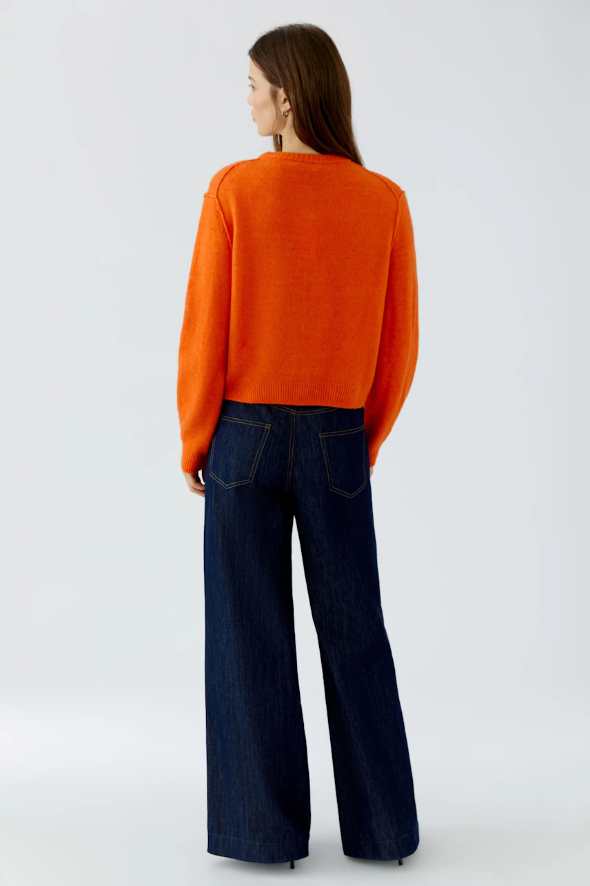 Frau in orangefarbener Strickjacke und blauer Jeans, Rückansicht. Lässiger Look für den Alltag.
