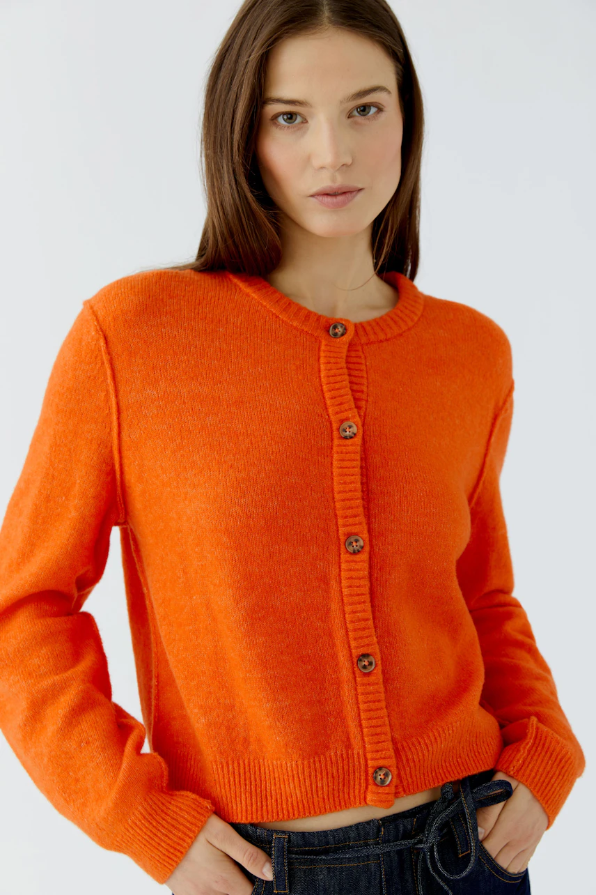 Strickjacke: Frau in leuchtend orangefarbener Strickjacke mit Knopfleiste, lässig kombiniert mit Jeans.