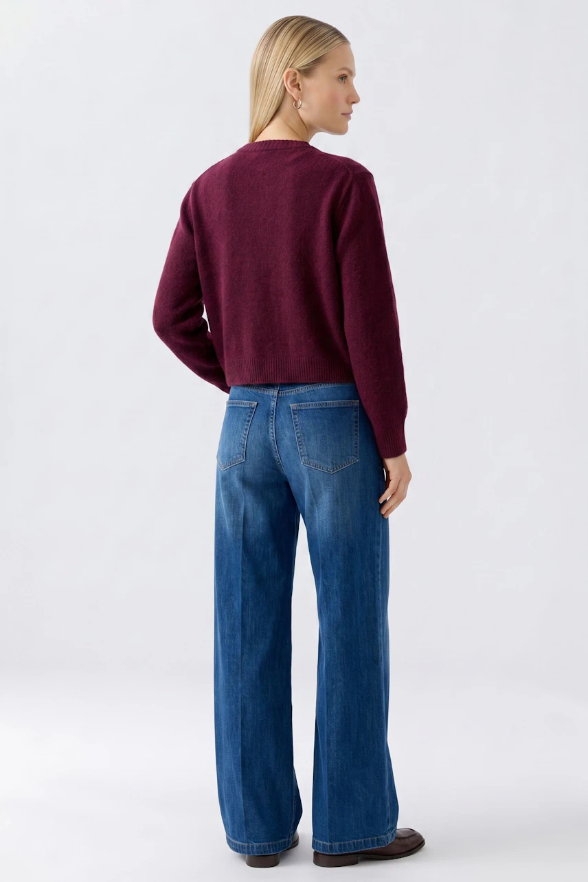 Damen-Strickjacke: Frau in bordeauxfarbener Strickjacke und lässigen Jeans von hinten.