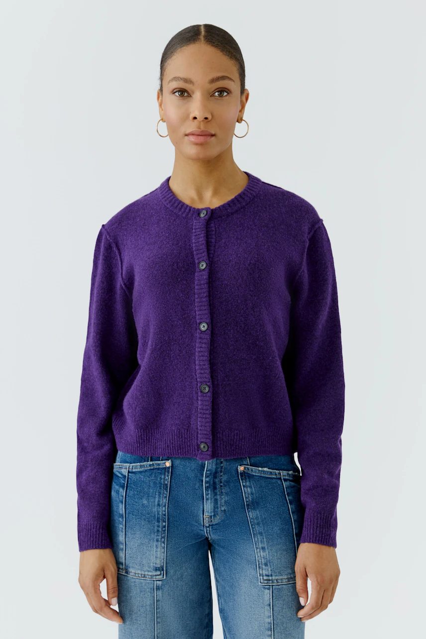 Casual cardigan: Woman in purple knit cardigan with button front, paired with blue jeans, standing confidently.