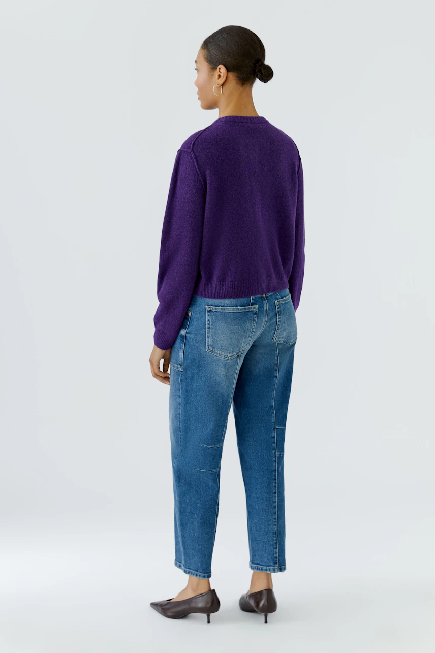 Casual cardigan: Woman in purple knit cardigan with blue jeans, standing confidently.