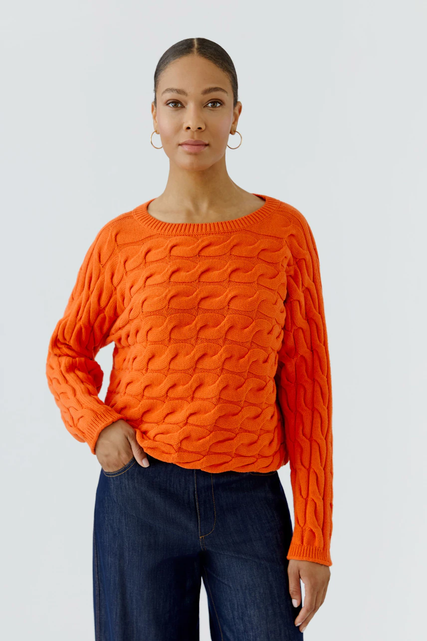 Casual women's pullover: Woman in vibrant orange textured pullover with relaxed fit, paired with dark jeans.