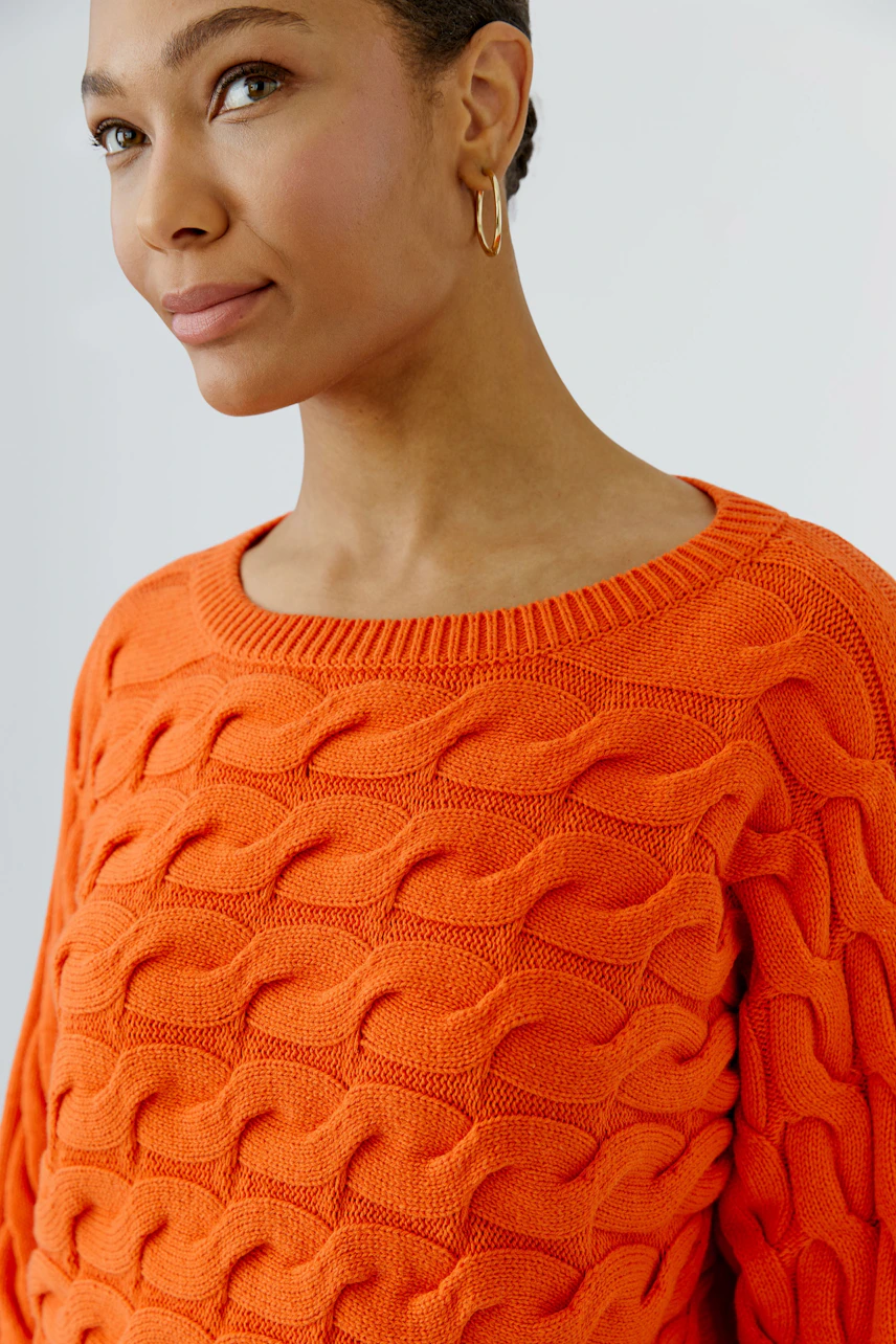 Woman in vibrant orange pullover with textured pattern, looking confidently to the side.