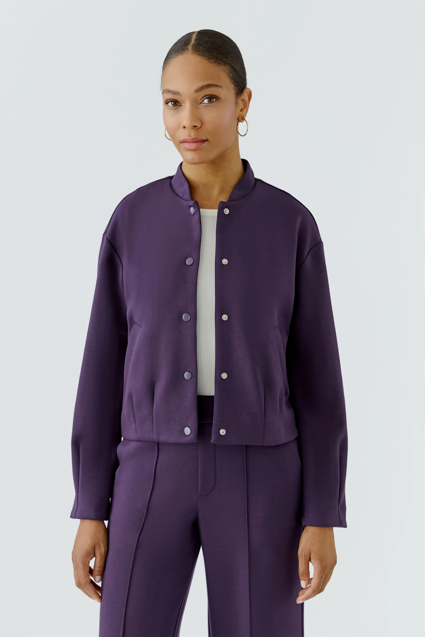Lässiger Damen-Blouson: Frau im lila Blouson mit Knopfleiste und passender Hose, schlicht und modern.