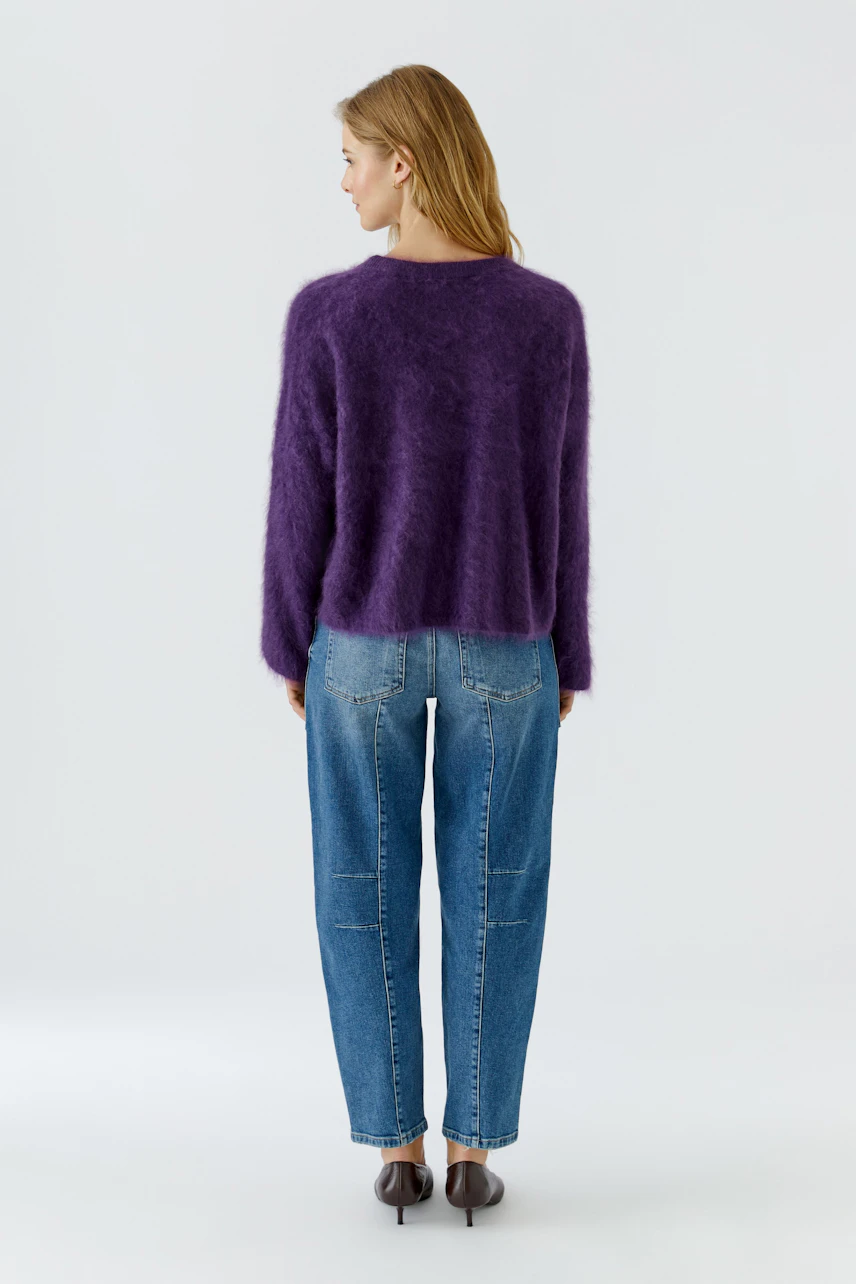 Frau im lila Pullover und blauer Jeans, von hinten gesehen. Lässiger Look für den Alltag.