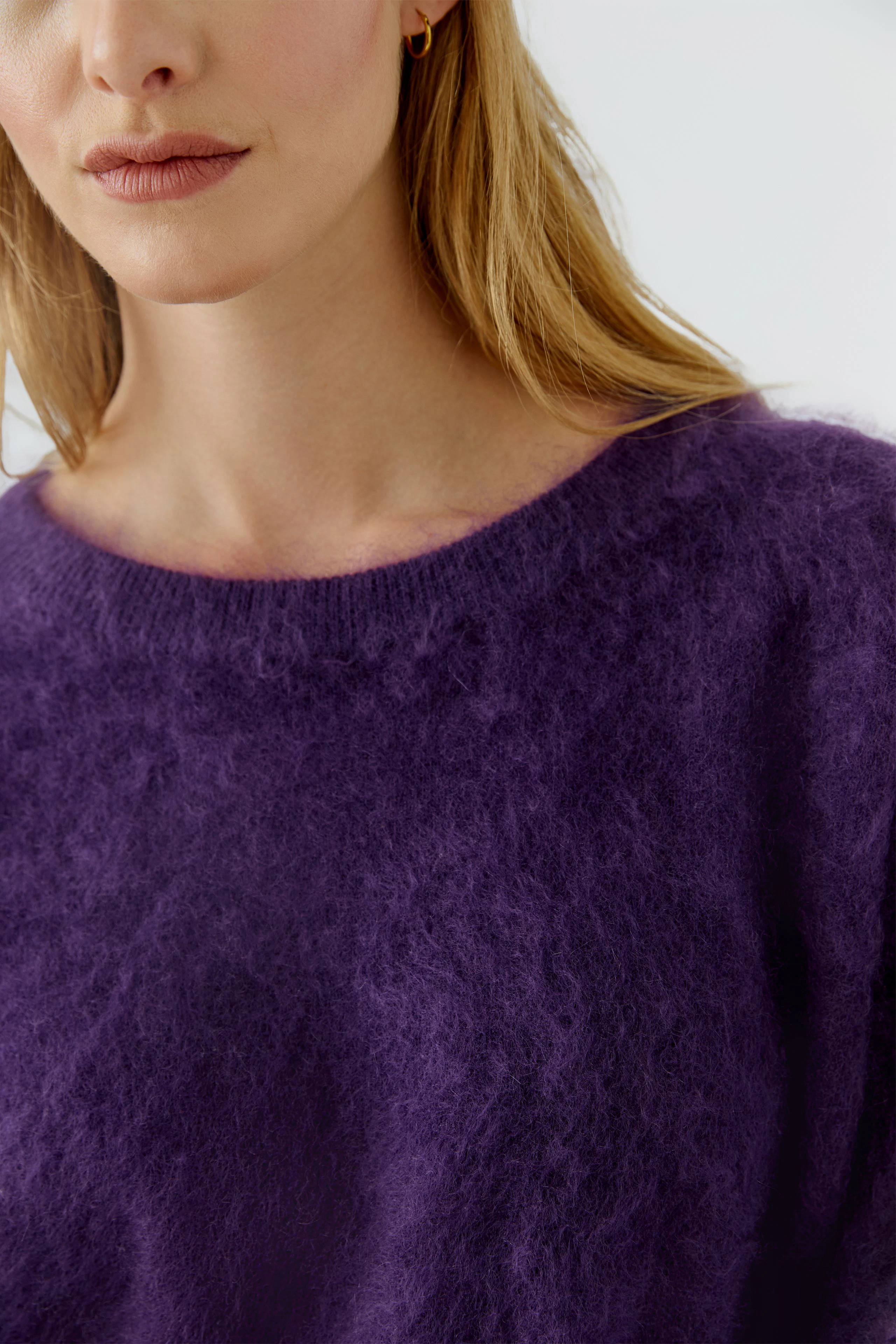 Frau im lila Pullover aus flauschigem Material, kombiniert mit blauen Jeans. Schlicht und modern.