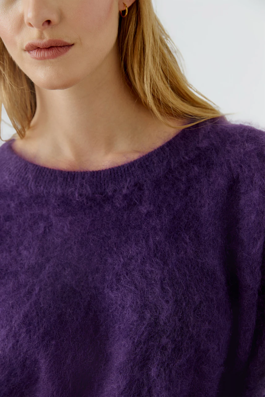 Frau im lila Pullover aus flauschigem Material, kombiniert mit blauen Jeans. Schlicht und modern.