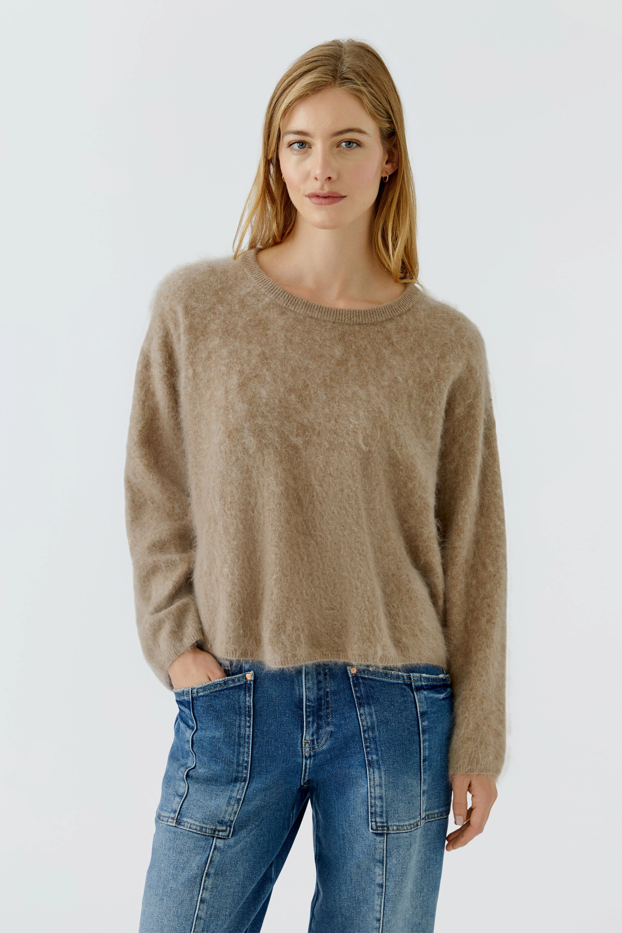 Damen-Pullover: Frau im flauschigen, beigen Pullover kombiniert mit gemusterten Hosen, lässiger Look.