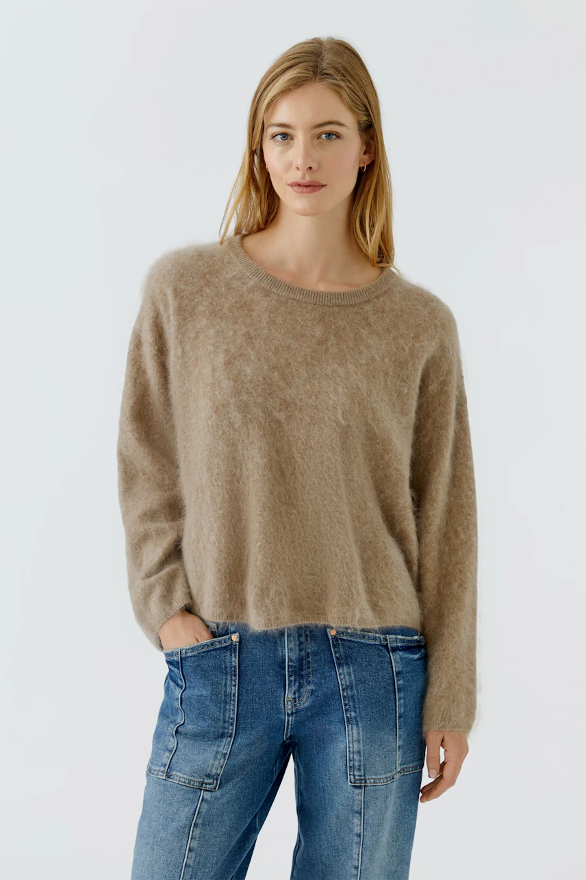 Damen-Pullover: Frau im flauschigen, beigen Pullover kombiniert mit gemusterten Hosen, lässiger Look.