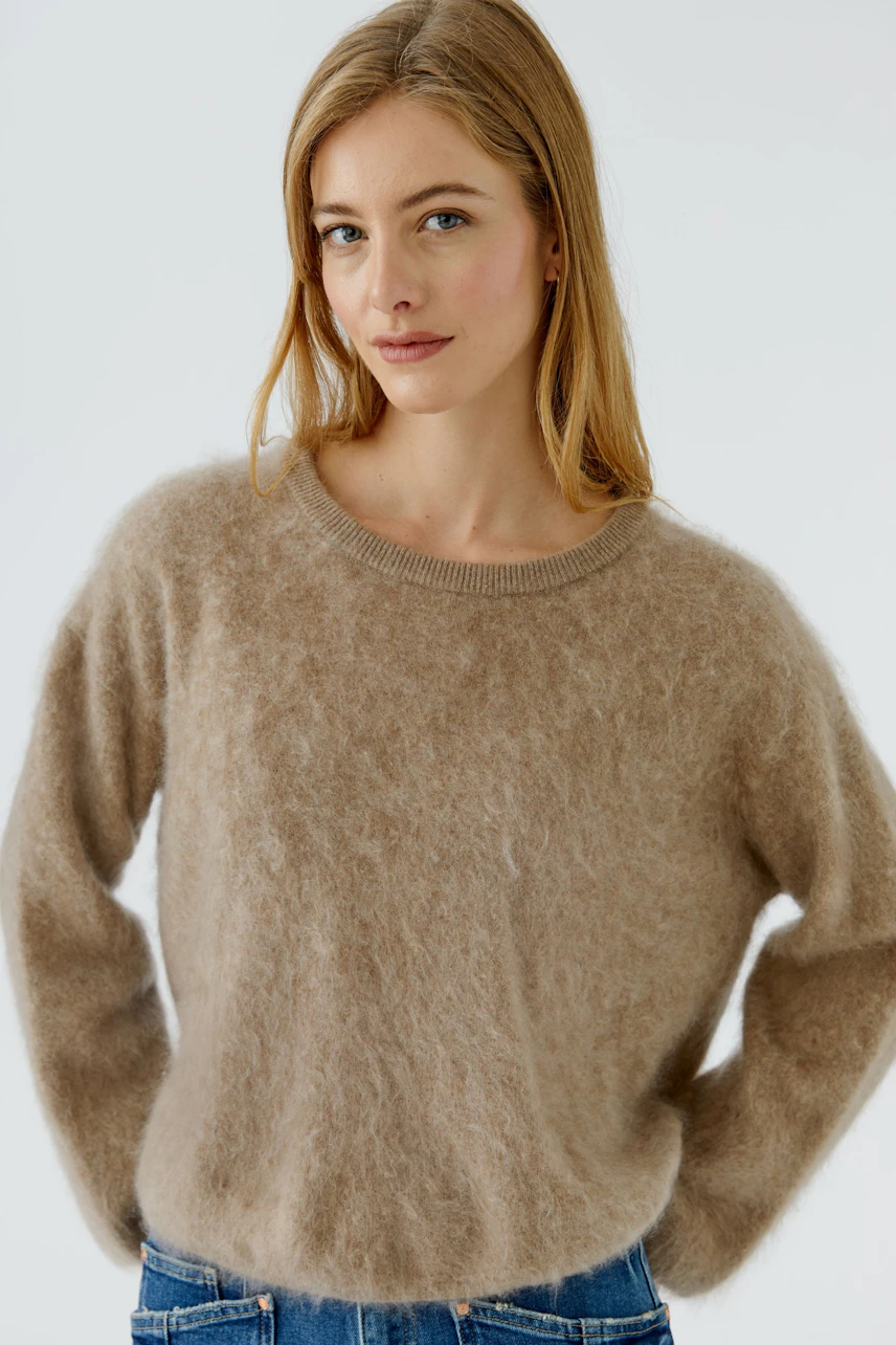 Casual women's pullover: Woman in a soft beige pullover with relaxed fit, paired with blue jeans.